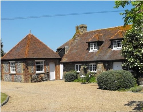 Two brick built cottages with tiled roofs and gravel path in front. Trees and bushes to right of image