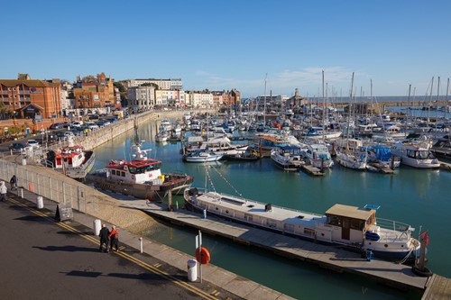 Looking across boats and yachts in harbour. Road and buildings  surrounding harbour